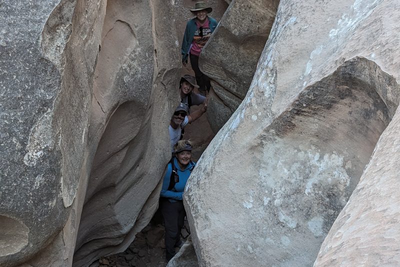 Hikers in single file squeezing through the pale, sculpted walls of the Utah Slots